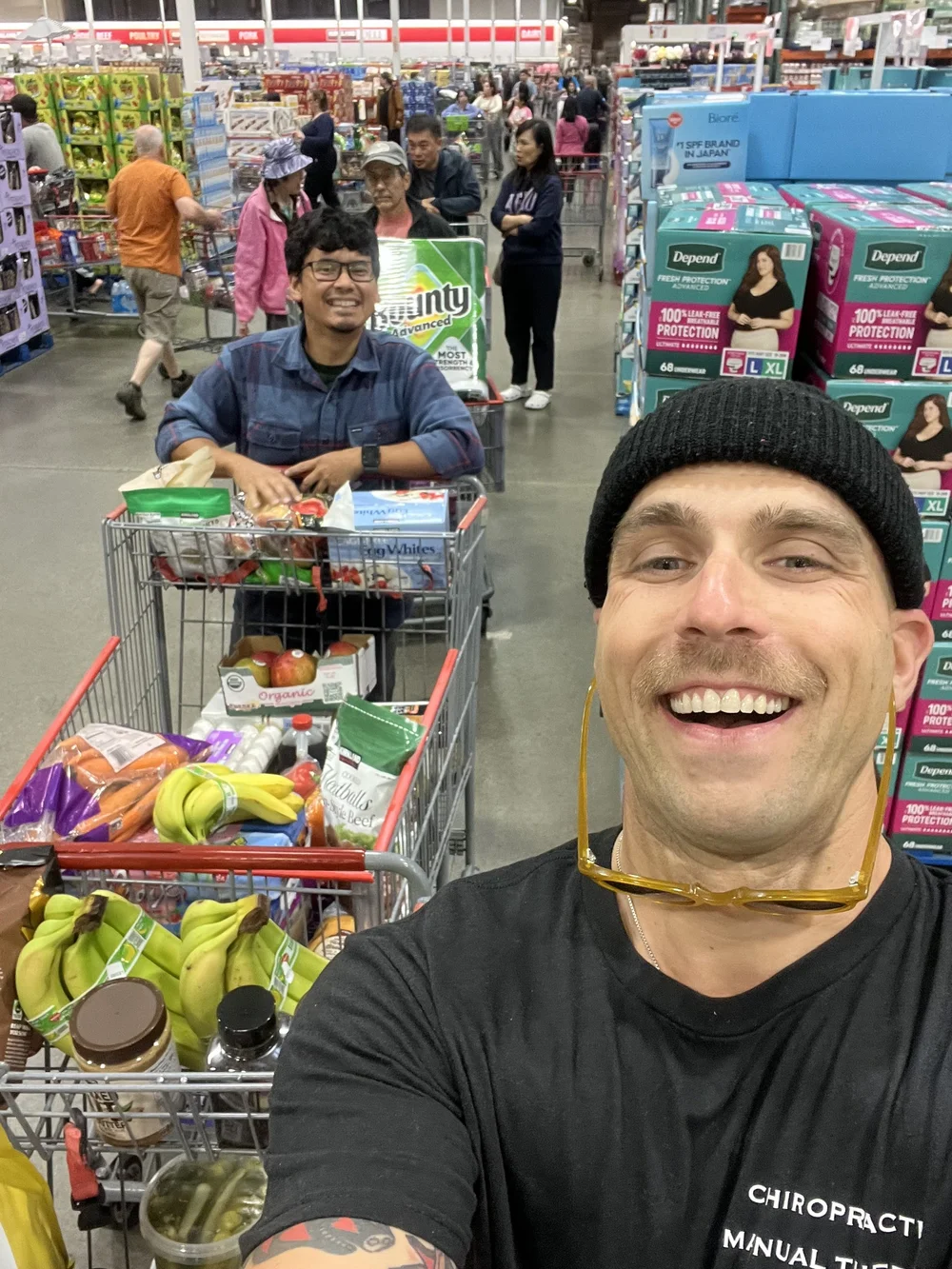 Two shoppers with carts full of fresh produce and groceries at Costco.